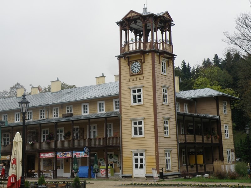 Naprzeciwko - BAZAR, okazały drewniany, dwupiętrowy obiekt zbudowany został w latach 1876–1880; widoczna na wieży tarcza zegarowa 